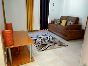 Un salon avec un canapé, un tapis à motifs et une table sur laquelle se trouve une bobine de fil.