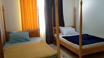 Una stanza con due letti in legno, uno con poggiatesta e uno senza, una finestra con tende e un pavimento piastrellato.