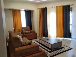 Un saló amb un sofà, una taula de centre i una televisió. Hi ha cortines a les finestres.