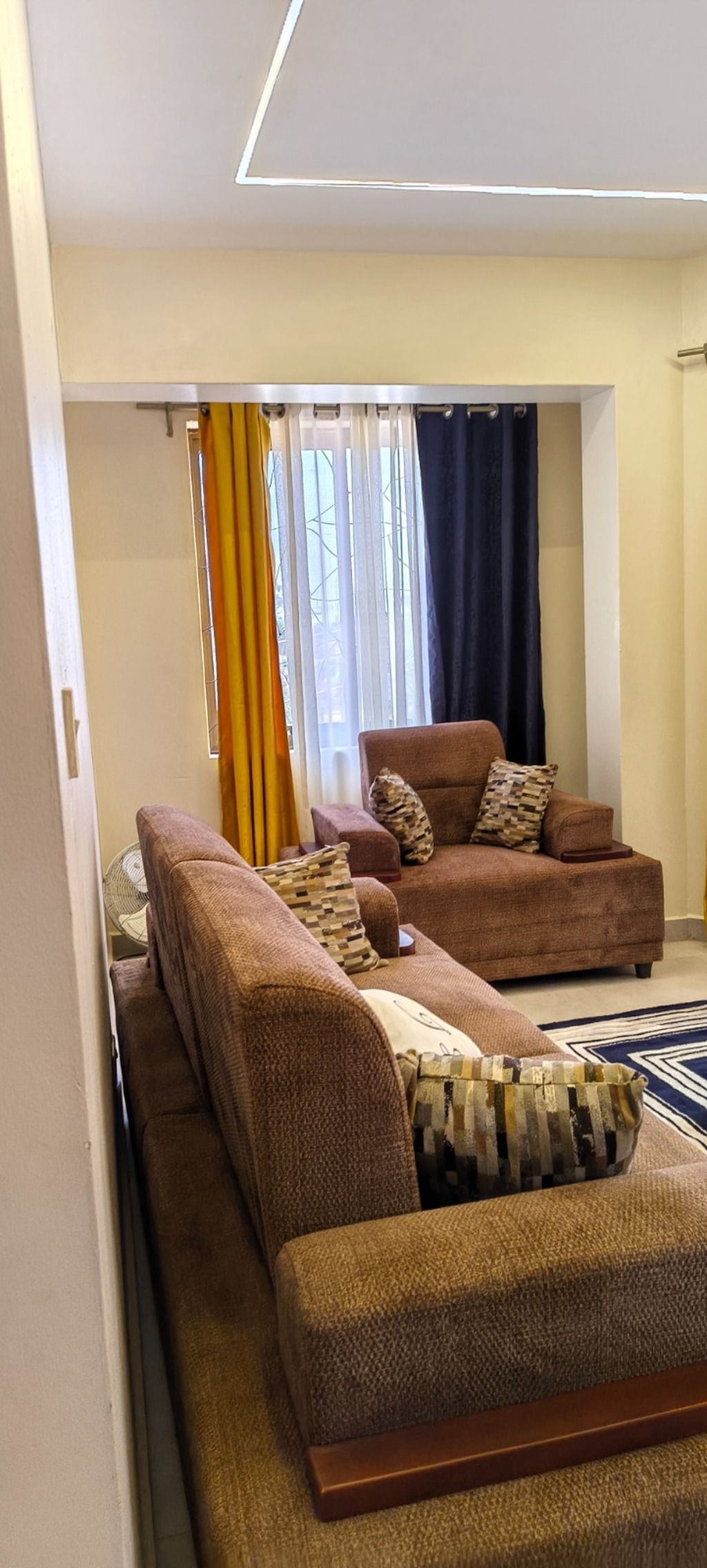 A living room with a sofa set and a small table, a window with curtains, and a carpeted floor.