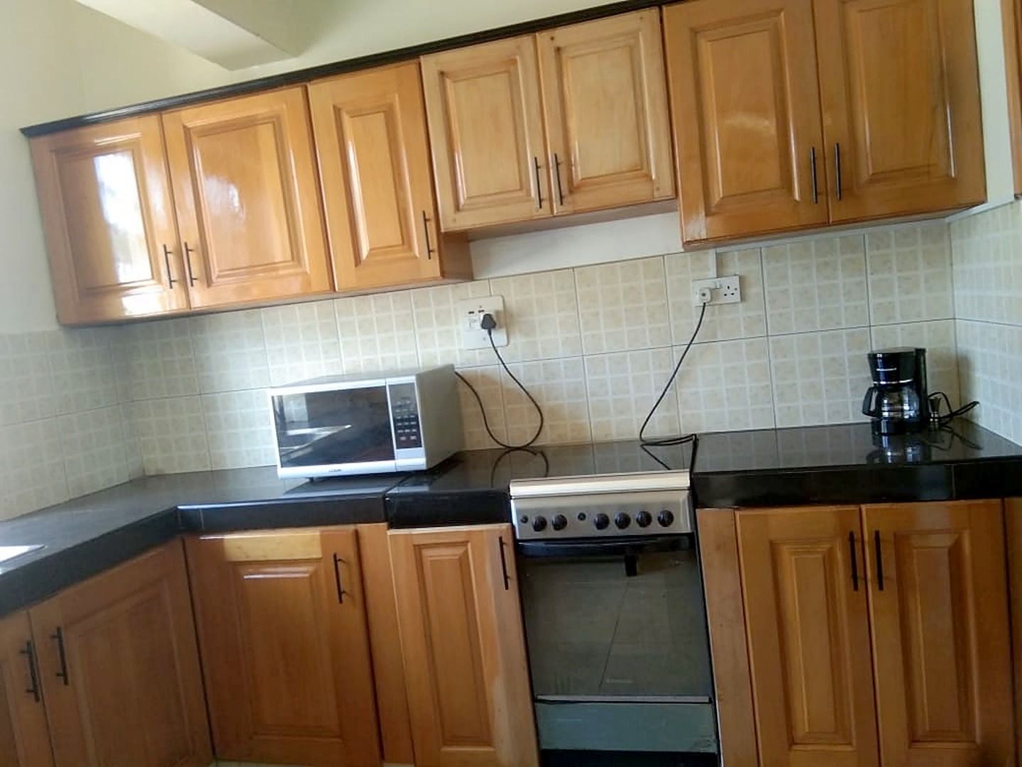 Una cocina con armarios de madera, microondas, estufa y cafetera.