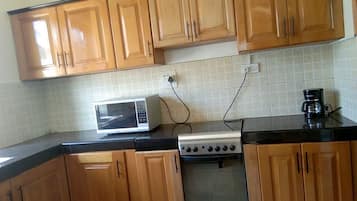 Una cocina con armarios de madera, microondas, estufa y cafetera.