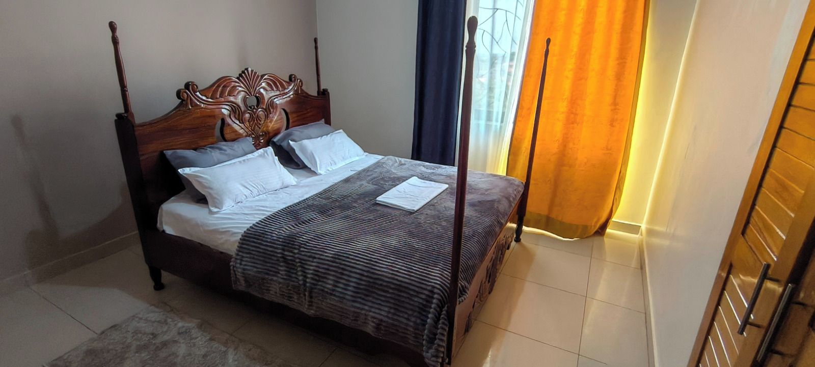 A four-poster bed with a dark wooden headboard, white linens, and a striped blanket.