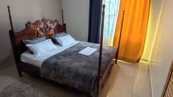 A four-poster bed with a dark wooden headboard, white linens, and a striped blanket.