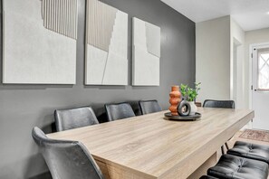 Een moderne eetruimte met een lange houten tafel, zwarte leren stoelen en een grijze accentmuur met abstracte kunst.
