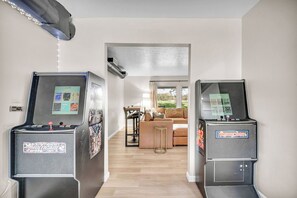 A hallway with arcade machines on either side leading to a living area with a sofa and a table. - Air Hockey + Shuffleboard | 3BR Near CLE (Berea)