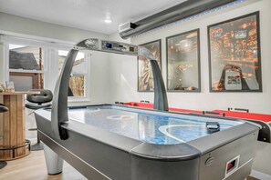 A pool table with a modern design, a bar area with a dartboard, and framed pictures on the wall. - Air Hockey + Shuffleboard | 3BR Near CLE (Berea)