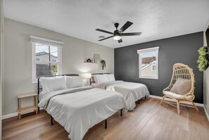 Een slaapkamer met twee bedden, een plafondventilator, een nachtkastje en een stoel.