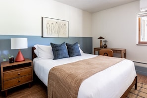 A neatly arranged hotel room with a bed, bedside table, lamp, and a framed artwork on the wall. - Cozy 2BR, Steps to Mines, Workspaces (Golden)
