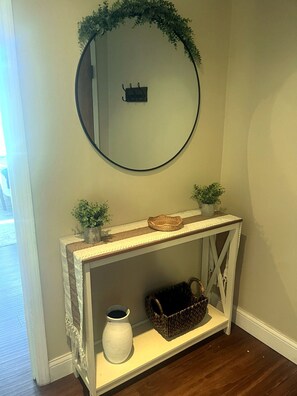 Een witte console tafel met een spiegel erboven, een klein plantje en een mand.