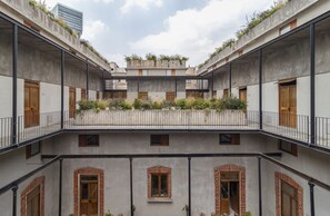 Pátio em vários níveis com varandas, algumas com vegetação, e um edifício moderno ao fundo.