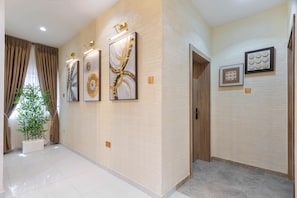A hallway with a modern design, featuring a large potted plant, abstract wall art, and a door leading to another room. - Luxury 2BR in Lagos  Wood-Slat Accent Design, AC & Modern Comfort (Lagos)