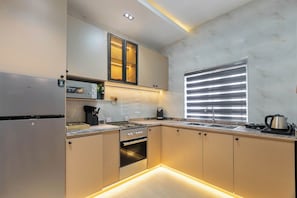 A modern kitchen with a built-in oven, stainless steel appliances, and a window with blinds. - Luxury 2BR in Lagos  Wood-Slat Accent Design, AC & Modern Comfort (Lagos)