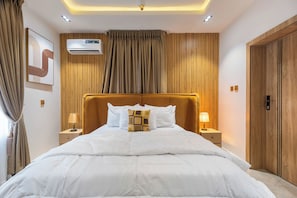 A hotel room with a large bed, two bedside tables with lamps, a wooden headboard, and a wooden wardrobe. - Luxury 2BR in Lagos  Wood-Slat Accent Design, AC & Modern Comfort (Lagos)