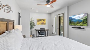 A modern bedroom with a bed, desk, chair, television, and a door leading to a bathroom. - Deer Mountain Retreat 3bdr townhouse near Fall RiverRocky Mountain National Park (Estes Park)