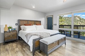 A bedroom with a large bed, wooden headboard, and a view of a mountainous landscape through a sliding door. - Deer Mountain Retreat 3bdr townhouse near Fall RiverRocky Mountain National Park (Estes Park)