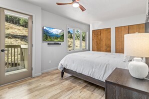 A bedroom with a bed, a ceiling fan, a TV, and a view of the outdoors. - Deer Mountain Retreat 3bdr townhouse near Fall RiverRocky Mountain National Park (Estes Park)