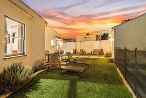 Ein Garten mit Kunstrasen, Gartenmöbeln und einem Sonnenuntergangshimmel.