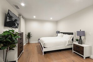 Ein Schlafzimmer mit einem Bett, Nachttischen, einer Kommode, einem Fernseher und einer Topfpflanze.