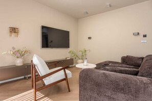 A modern living room with a flat-screen TV, a sofa, a chair, and a small round table. - Villa Belo Krug – Heated Pool & Sea View (Jesenice)