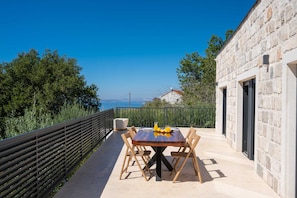An outdoor dining area with a table and chairs, a stone building, and a view of the sea. - Villa Belo Krug – Heated Pool & Sea View (Jesenice)