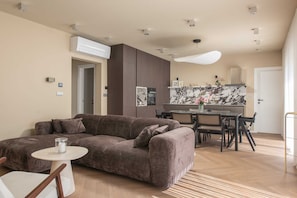 A modern living room with a sofa, a dining table, and chairs. There is a kitchen area with a marble countertop and cabinets. - Villa Belo Krug – Heated Pool & Sea View (Jesenice)