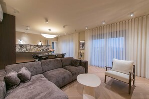 A modern living room with a sectional sofa, a small round table, and a white armchair. - Villa Belo Krug – Heated Pool & Sea View (Jesenice)