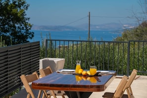 A dining table with chairs, a glass of orange juice, and a fruit plate. - Villa Belo Krug – Heated Pool & Sea View (Jesenice)
