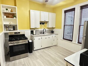 A compact kitchen with a gas stove, white cabinets, and a window with a mesh screen. - Entire Historic Elmwood Village 3BR APT - Amazing Location (Buffalo)