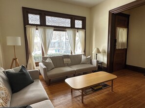 Un salon avec un canapé, une table basse et une lampe. Il y a des rideaux aux fenêtres.