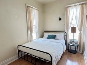 A single bed with a metal frame, white bedding, and a patterned pillow in a room with cream walls and wooden flooring. - Entire Historic Elmwood Village 3BR APT - Amazing Location (Buffalo)