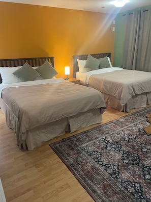 A hotel room with two beds, a nightstand with a lamp, a patterned rug, and a wooden floor. - Bayside Inn (Alert Bay)