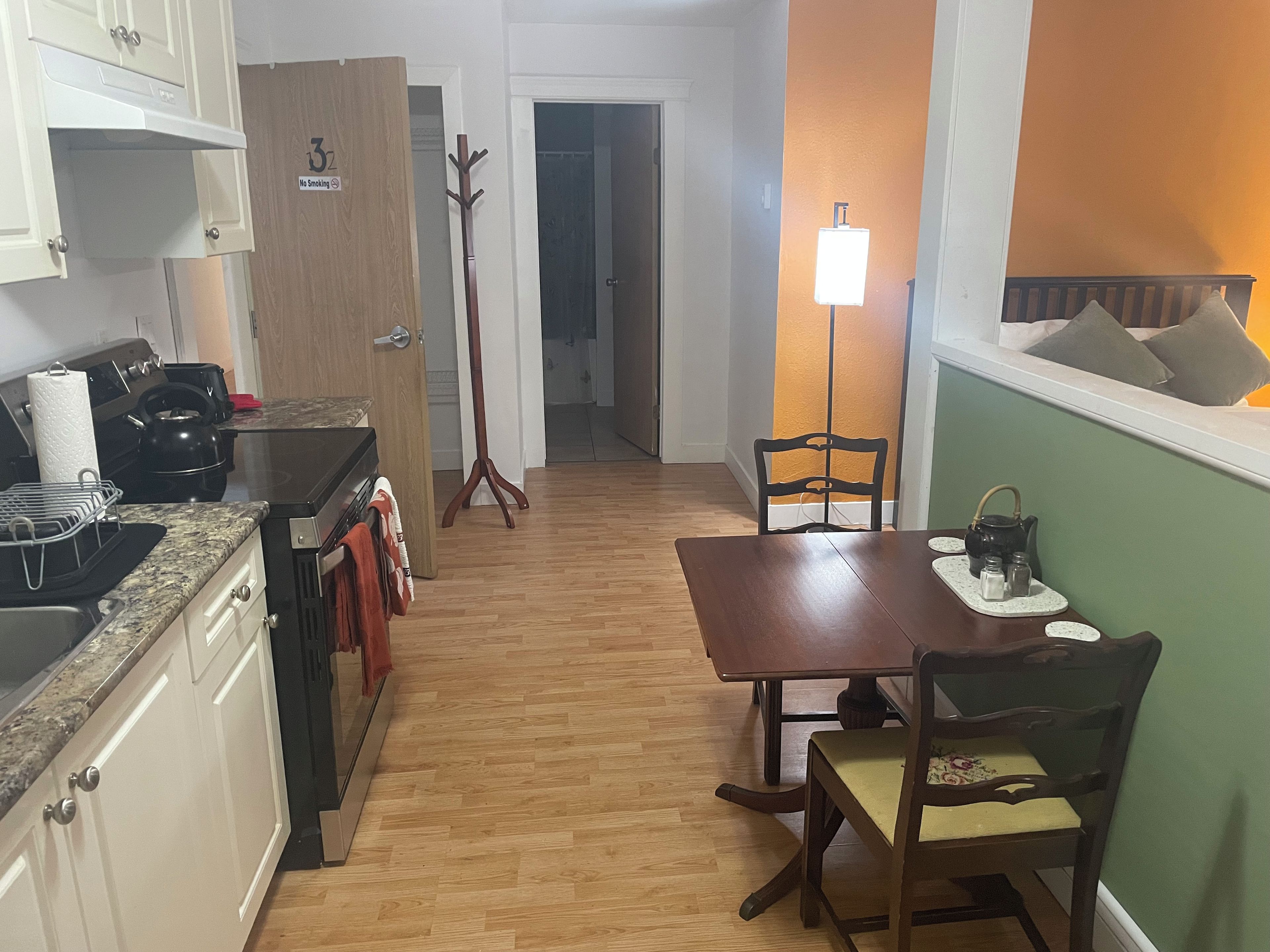 A compact kitchen with a dining area, wooden flooring, and a coat rack.