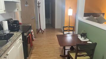 A compact kitchen with a dining area, wooden flooring, and a coat rack.