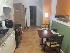A compact kitchen with a dining area, wooden flooring, and a coat rack. - Bayside Inn (Alert Bay)