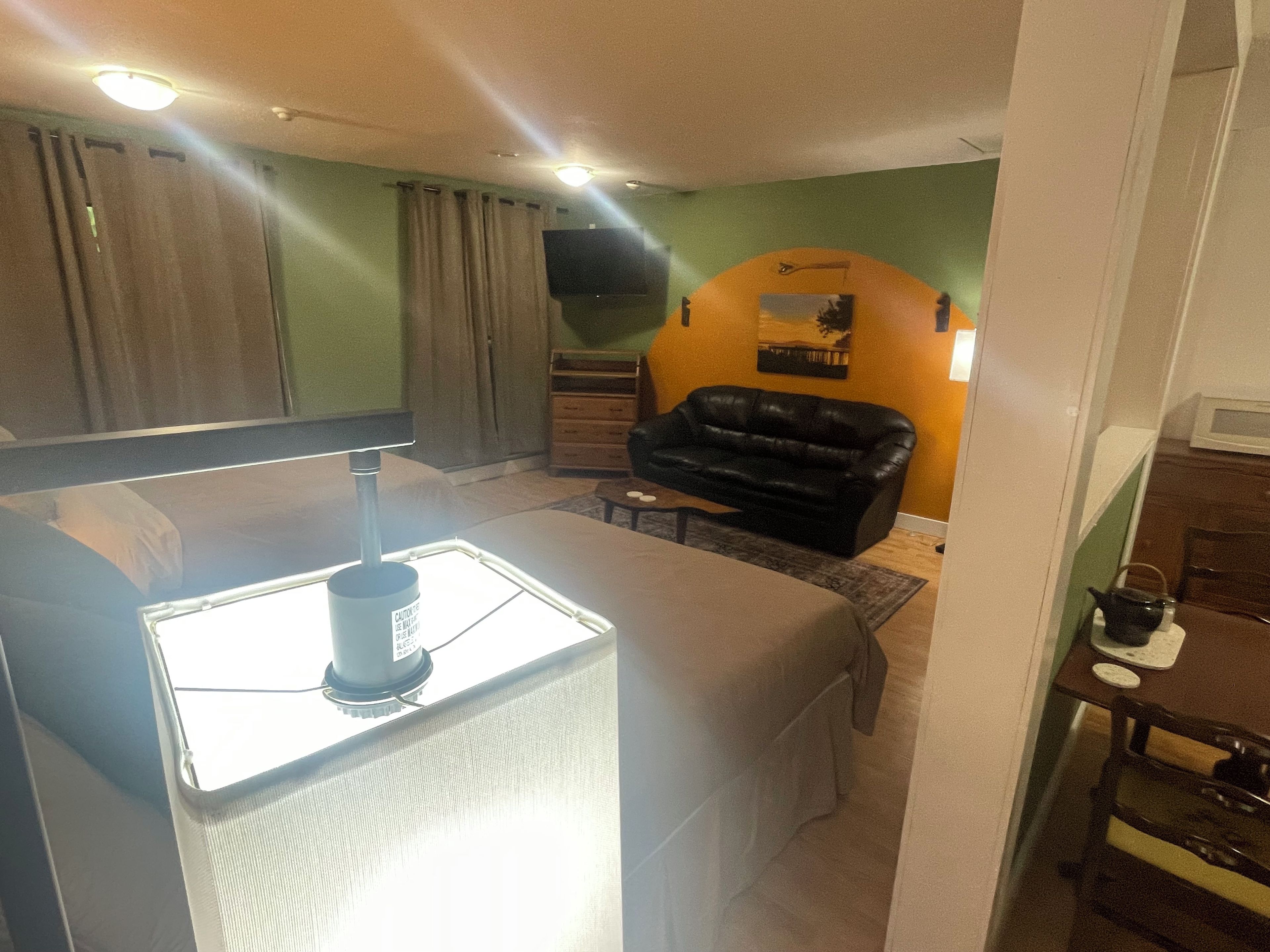 A compact living space with a kitchenette, a black leather sofa, and a flat-screen TV mounted on the wall.