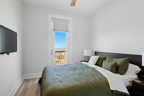 A bedroom with a bed, a TV mounted on the wall, a nightstand, and a window with a view. - Beachfront Paradise 3BR/3BA Park & Casino (Gulfport)