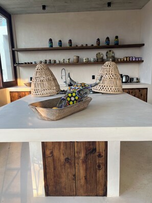 A kitchen with a central island, two hanging light fixtures, and shelves with various kitchenware. - Luxury Villa Xololo on the secluded beach of La Boquilla, Oaxaca, Pacific Coast (San Pedro Pochutla)