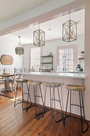 A modern kitchen with a bar area, wooden stools, and pendant lighting. - Southern Ease | 5BR Next to Cannon Green | Sleeps 10 (Charleston)