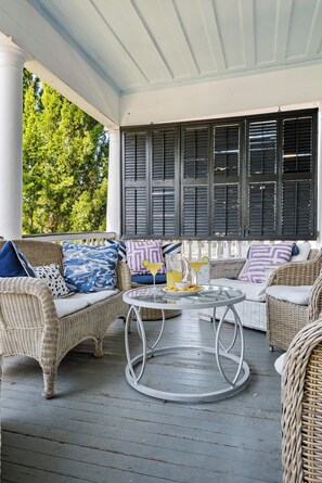 A covered porch with wicker furniture, a round table, and a view of trees. - Southern Ease | 5BR Next to Cannon Green | Sleeps 10 (Charleston)