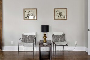 A room with two chairs with patterned cushions, a small table with a lamp, and two framed botanical illustrations on the wall. - Southern Ease | 5BR Next to Cannon Green | Sleeps 10 (Charleston)