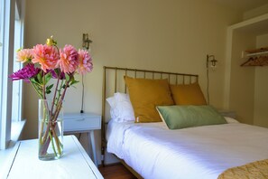 A hotel room with a bed, a nightstand, a vase with flowers, and a window. - Capitol Hill 2BR Gem - Stroll to Parks & Cafés (Seattle)