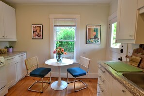 A kitchen with two blue chairs, a white table, and a window with greenery outside. - Capitol Hill 2BR Gem - Stroll to Parks & Cafés (Seattle)