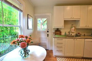 A kitchen with white cabinets, a dining table with a vase of flowers, and a view of greenery through the window. - Capitol Hill 2BR Gem - Stroll to Parks & Cafés (Seattle)