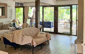 A living room with a covered sofa, a lamp, and a view of an outdoor patio area. - Superbe maison d'architecte (Cap Ferret)