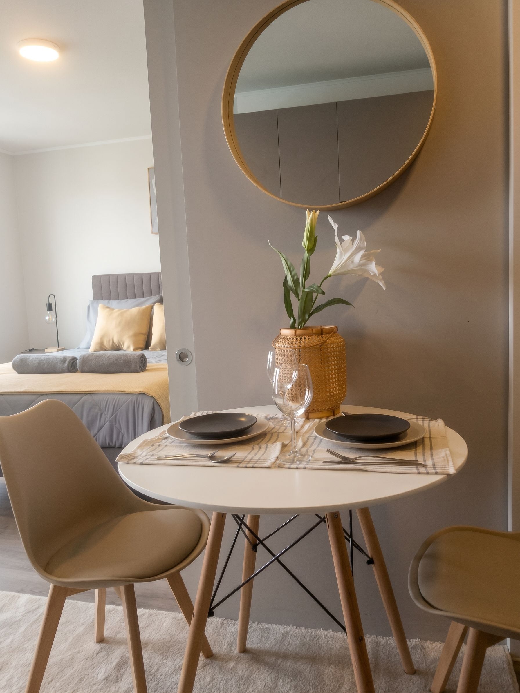Un comedor con una mesa redonda, sillas, un florero con flores y un espejo en la pared.