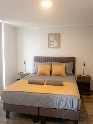 A bedroom with a bed, two bedside tables, a nightstand, a wall-mounted light, and a framed picture. - Edificio Froilan Lagos by Domus Travels (La Florida)