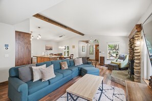 A spacious living area with a blue sectional sofa, wooden flooring, and a stone fireplace. - Homewood Cabin  - Walk to the Lake - Pet Friendly (Homewood)