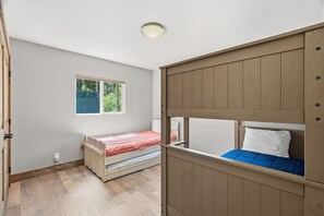 Ein Zimmer mit einem Etagenbett, einem Einzelbett, einem Fenster und einer Deckenleuchte.