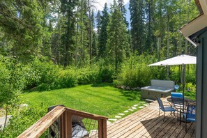 A deck with outdoor furniture, a hot tub, and a view of a forested area. - Homewood Cabin  - Walk to the Lake - Pet Friendly (Homewood)